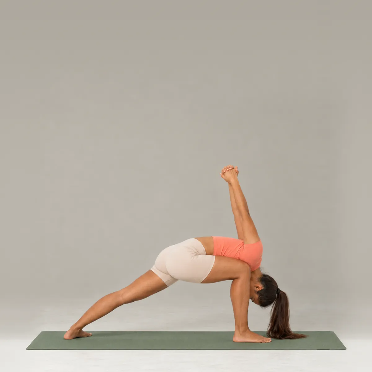 A woman in humble warrior on a green yoga mat, folding inside her front knee with hands clasped behind her back
