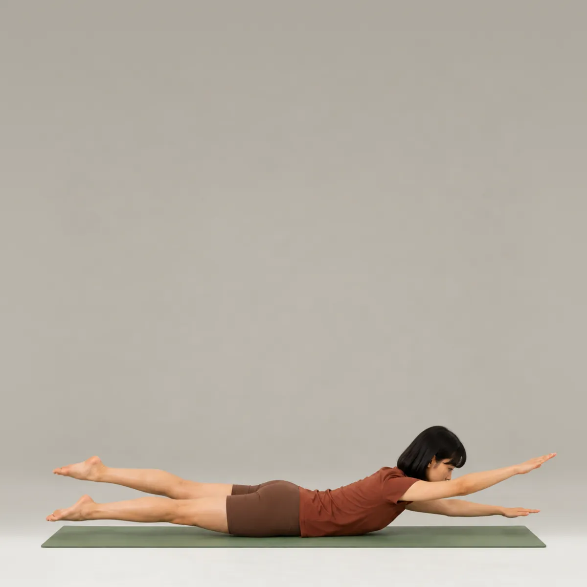 A woman doing pilates swimming on a green mat, lying face down with arms and legs lifted