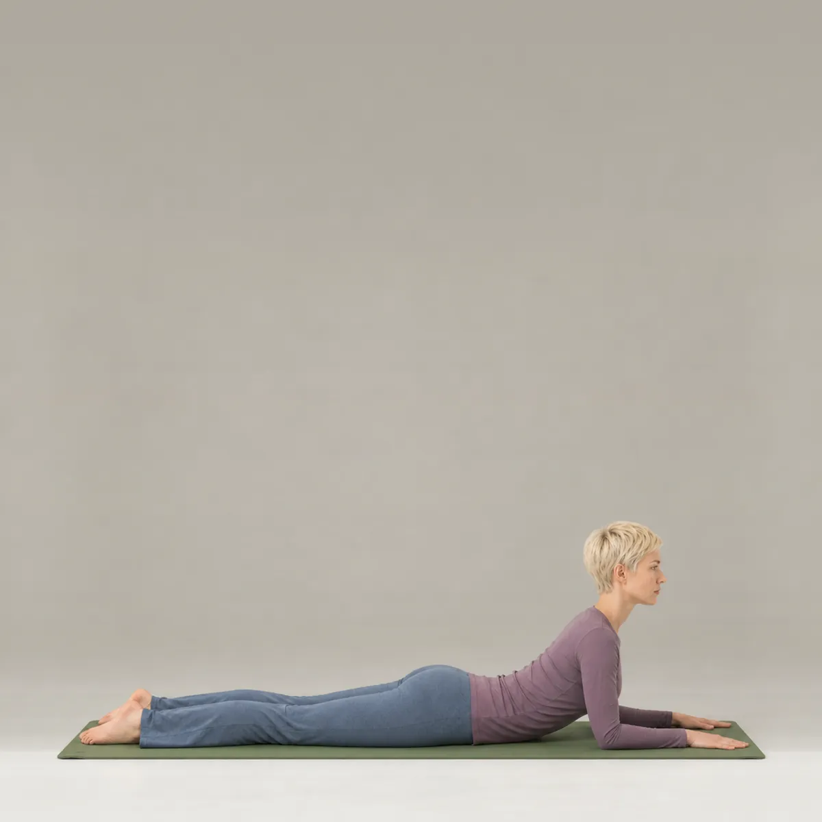 A woman in sphinx pose on a green yoga mat, lying face down and propped on her forearms