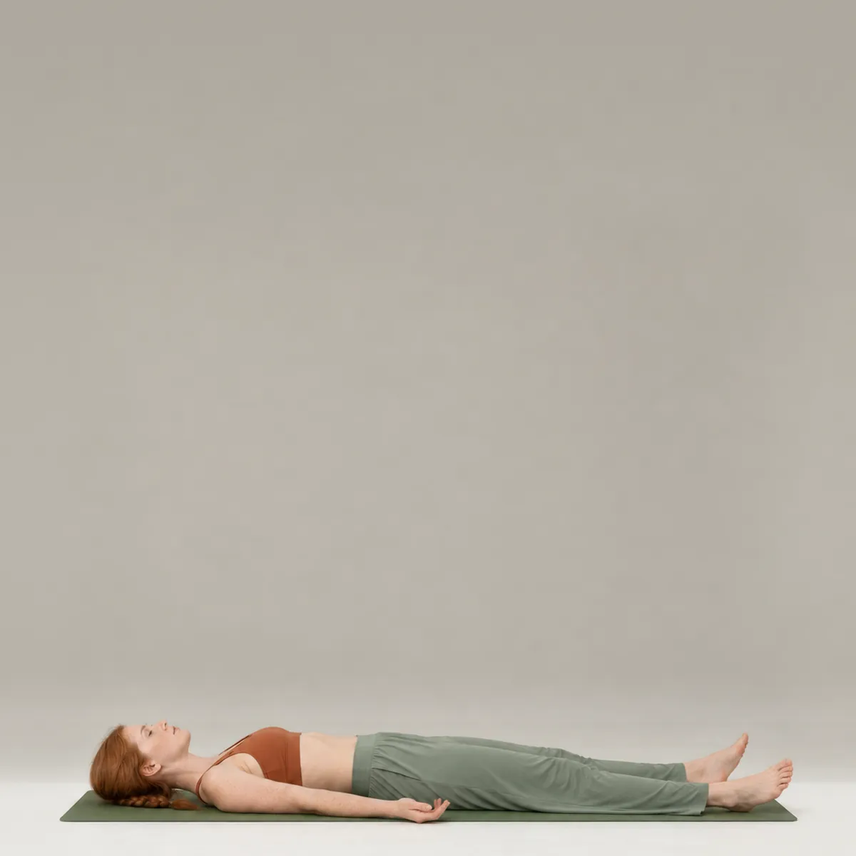 A woman resting in corpse pose on a green yoga mat, lying flat on her back