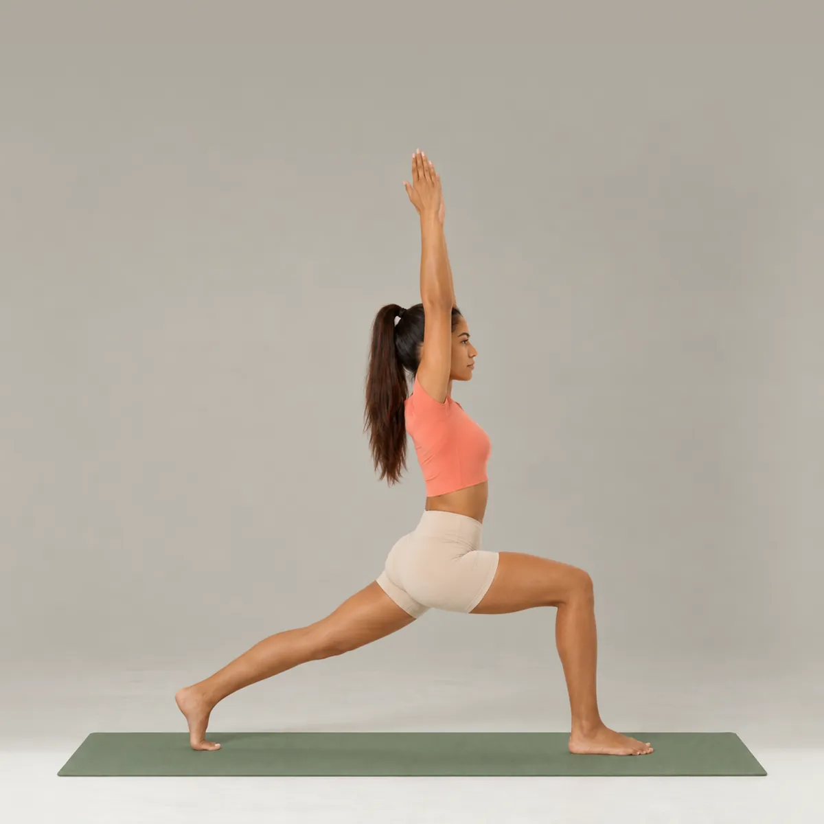 A woman in crescent lunge on a green yoga mat, back heel lifted and arms reaching overhead