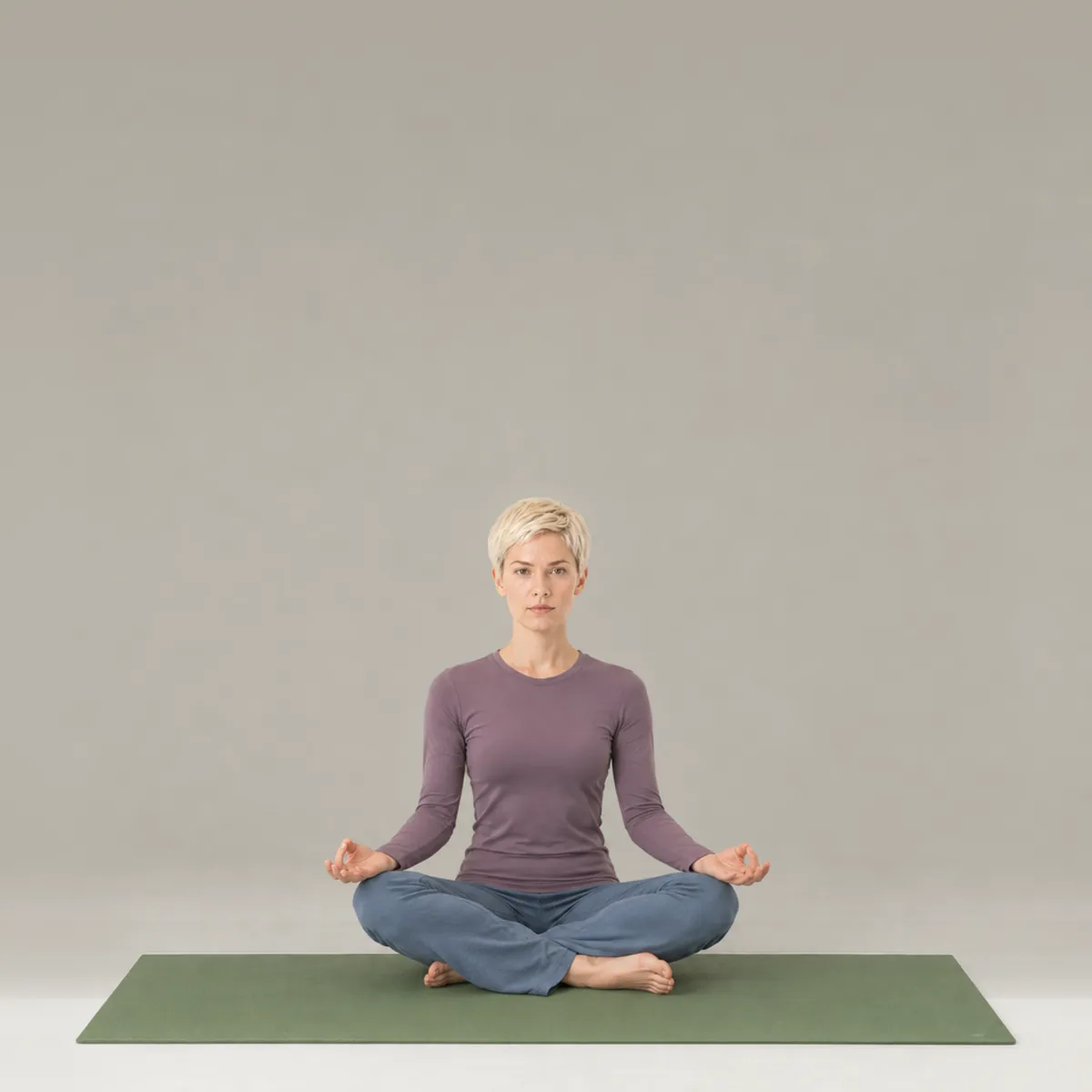 A woman sitting cross-legged in easy pose on a green yoga mat, hands resting on her knees