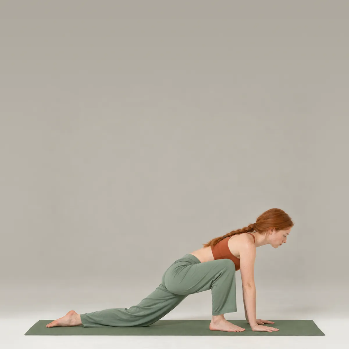 A woman in lizard pose on a green yoga mat, hands inside her front foot and back knee down