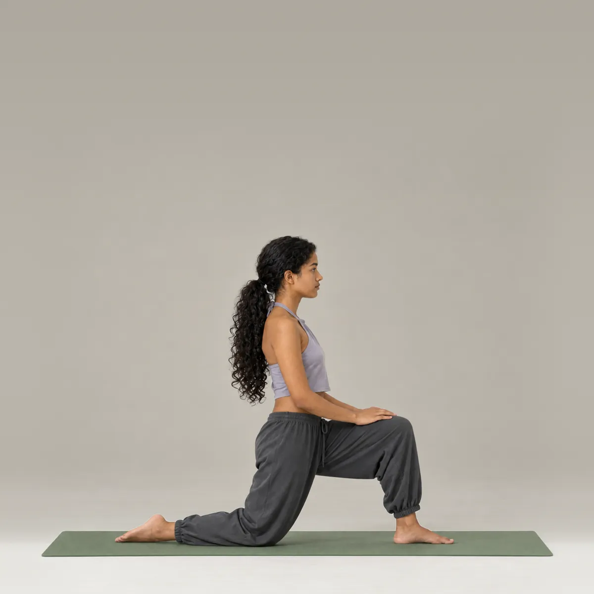 A woman in a low lunge on a green yoga mat, back knee down and torso upright