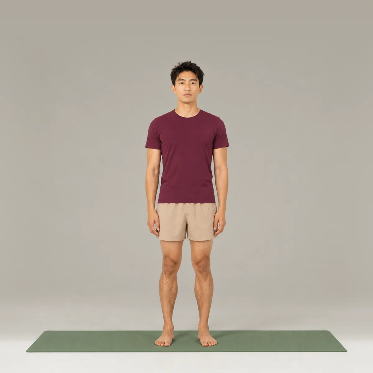 A man standing tall in mountain pose on a green yoga mat, arms relaxed by his sides