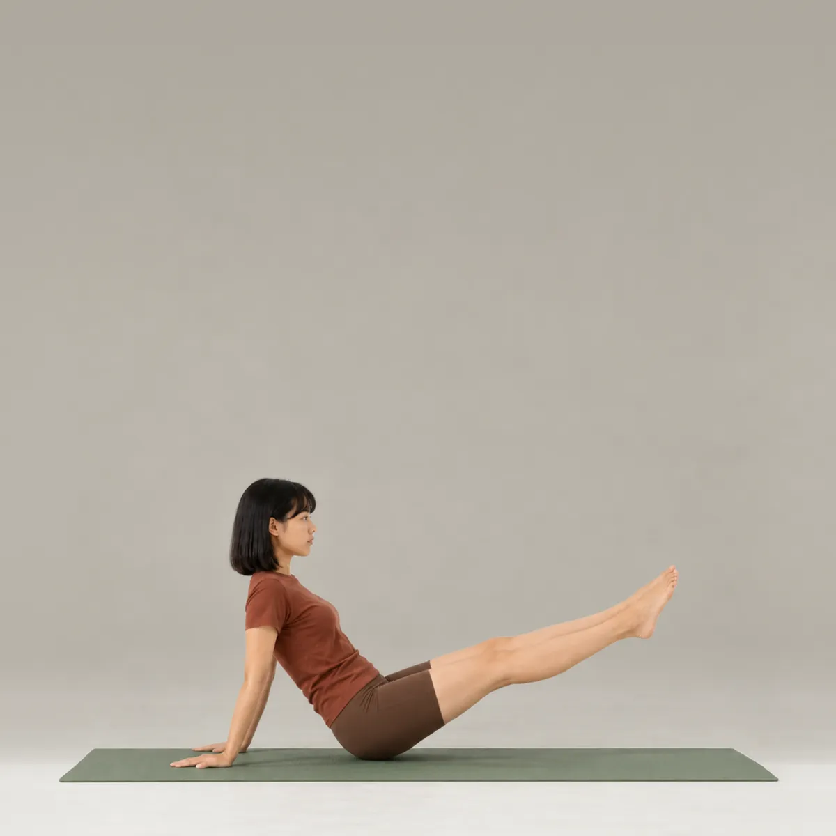 A woman doing the pilates hip twist on a green mat, leaning back on her hands with legs lifted