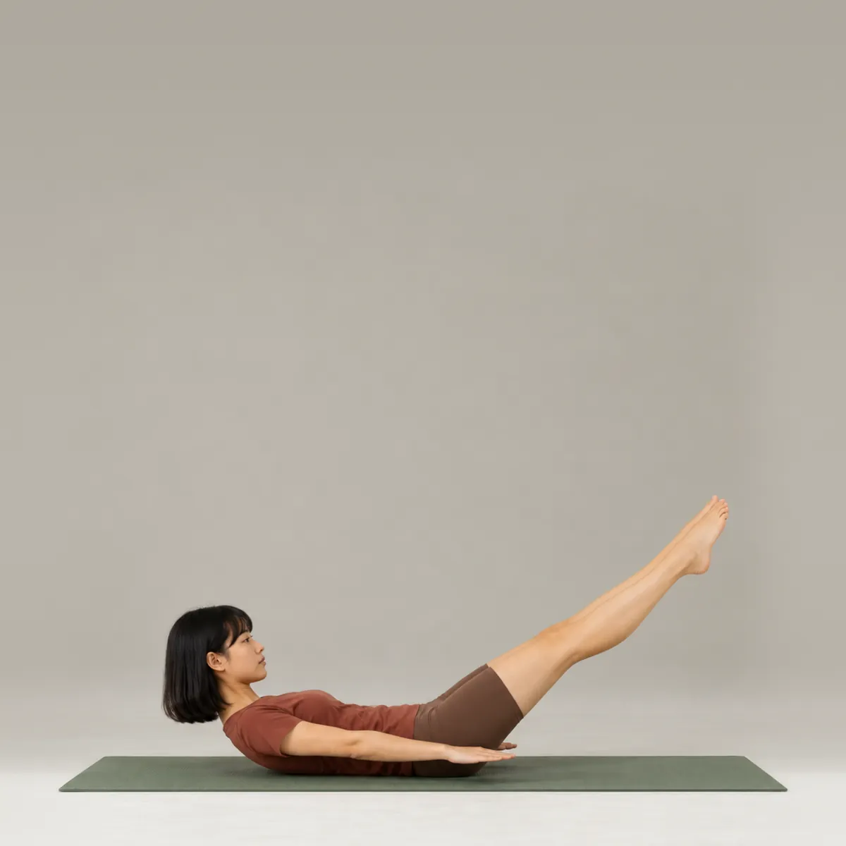 A woman doing the pilates hundred on a green mat, legs extended on a diagonal and arms long by her sides