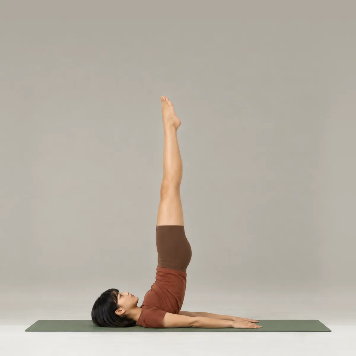 A woman doing the pilates jackknife on a green mat, legs reaching straight up from her shoulders
