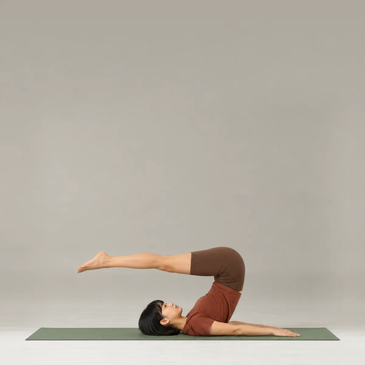 A woman doing the pilates roll over on a green mat, hips lifted and legs reaching over her head