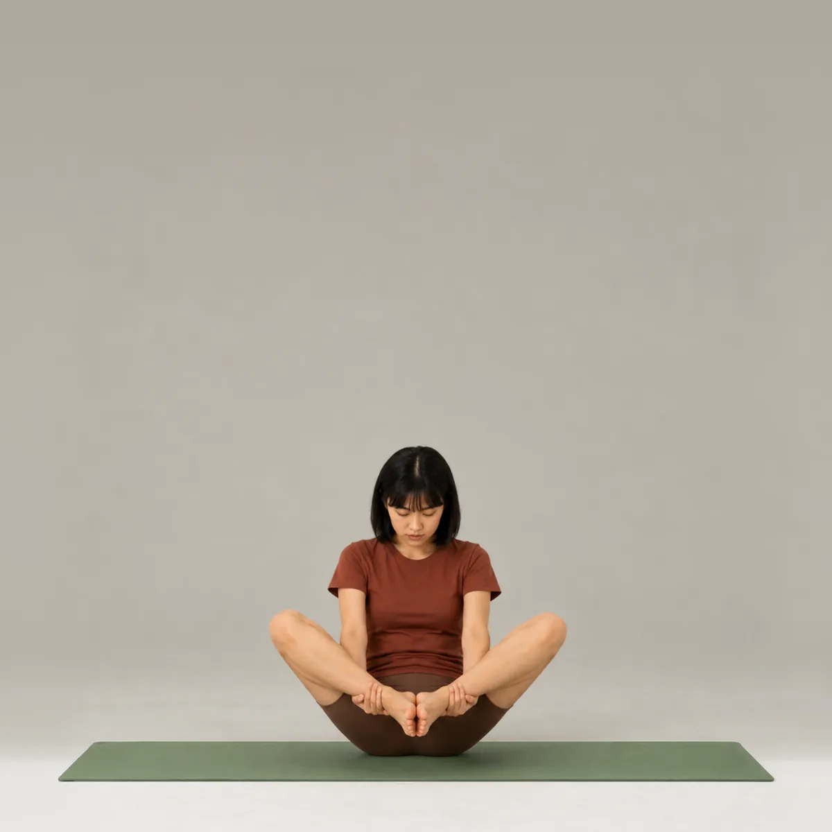 A woman balancing in the pilates seal on a green mat, holding her ankles with knees open