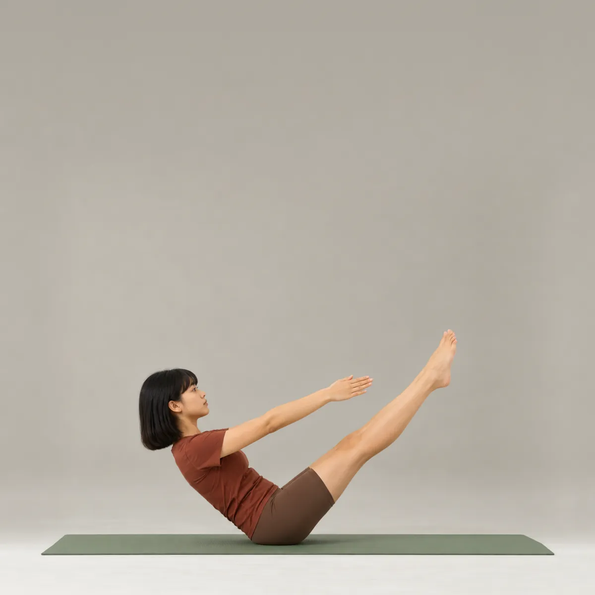 A woman balancing in the pilates teaser on a green mat, legs and arms reaching on a diagonal
