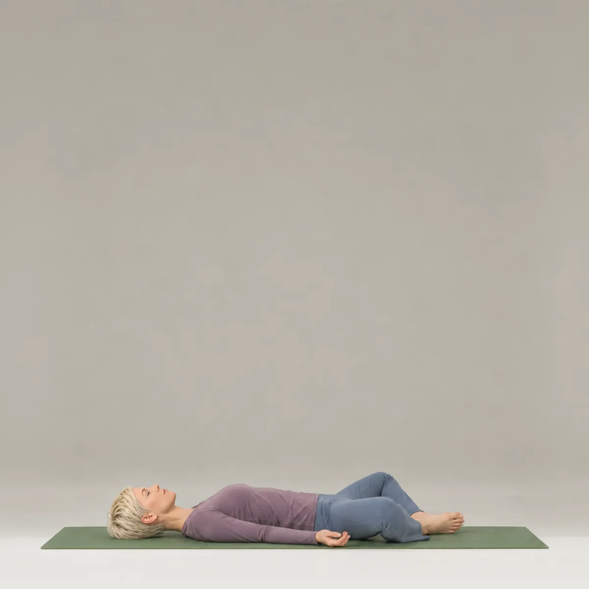 A woman lying on her back on a green yoga mat with the soles of her feet together and knees open