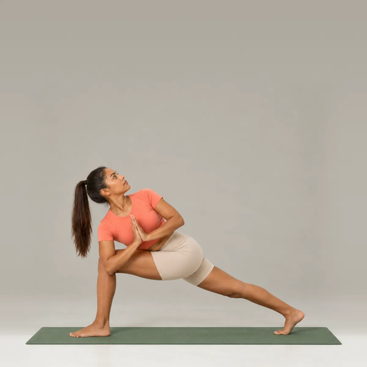 A woman in revolved side angle on a green yoga mat, twisting over her front knee with palms together