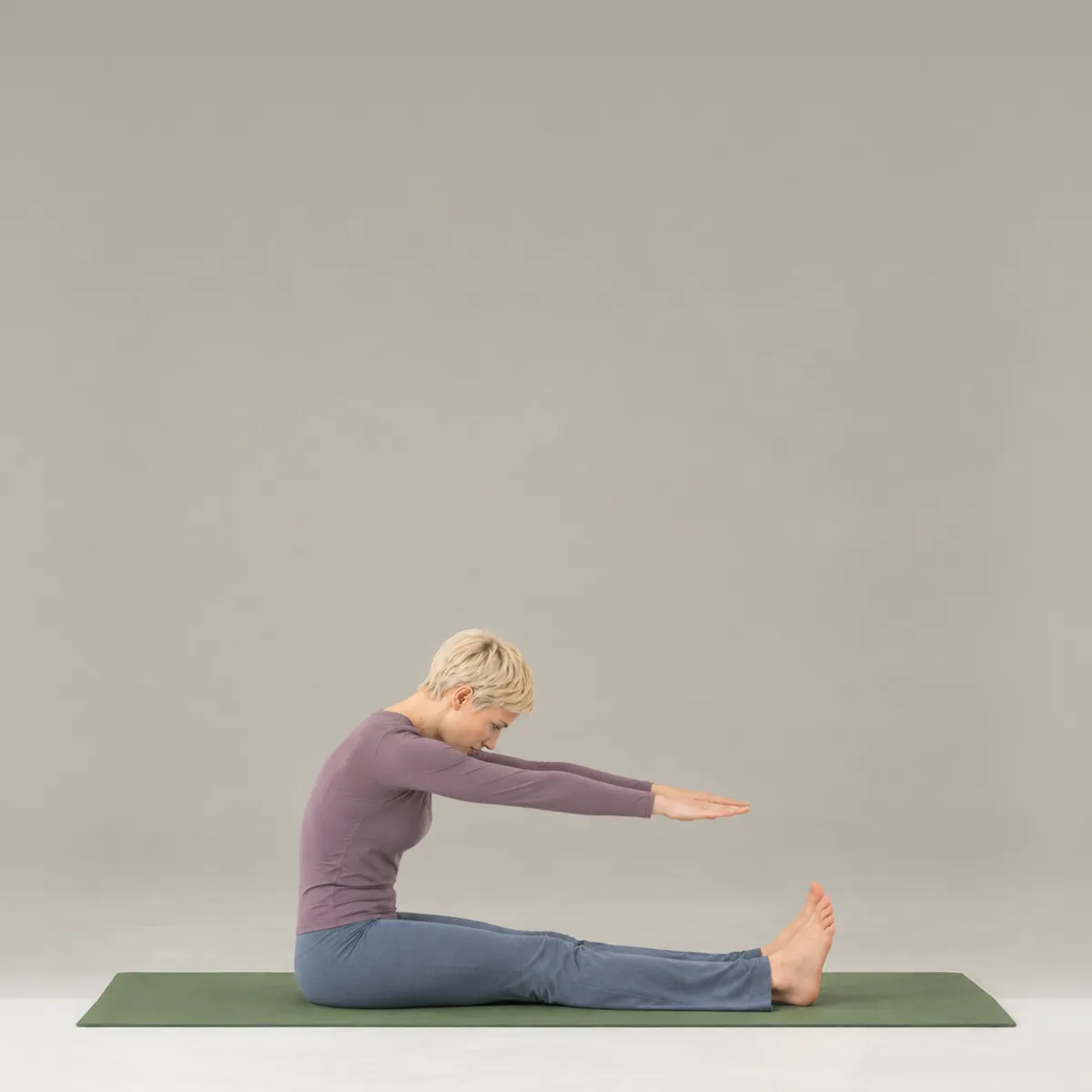 A woman doing spine stretch forward on a green mat, seated with legs long and arms reaching forward
