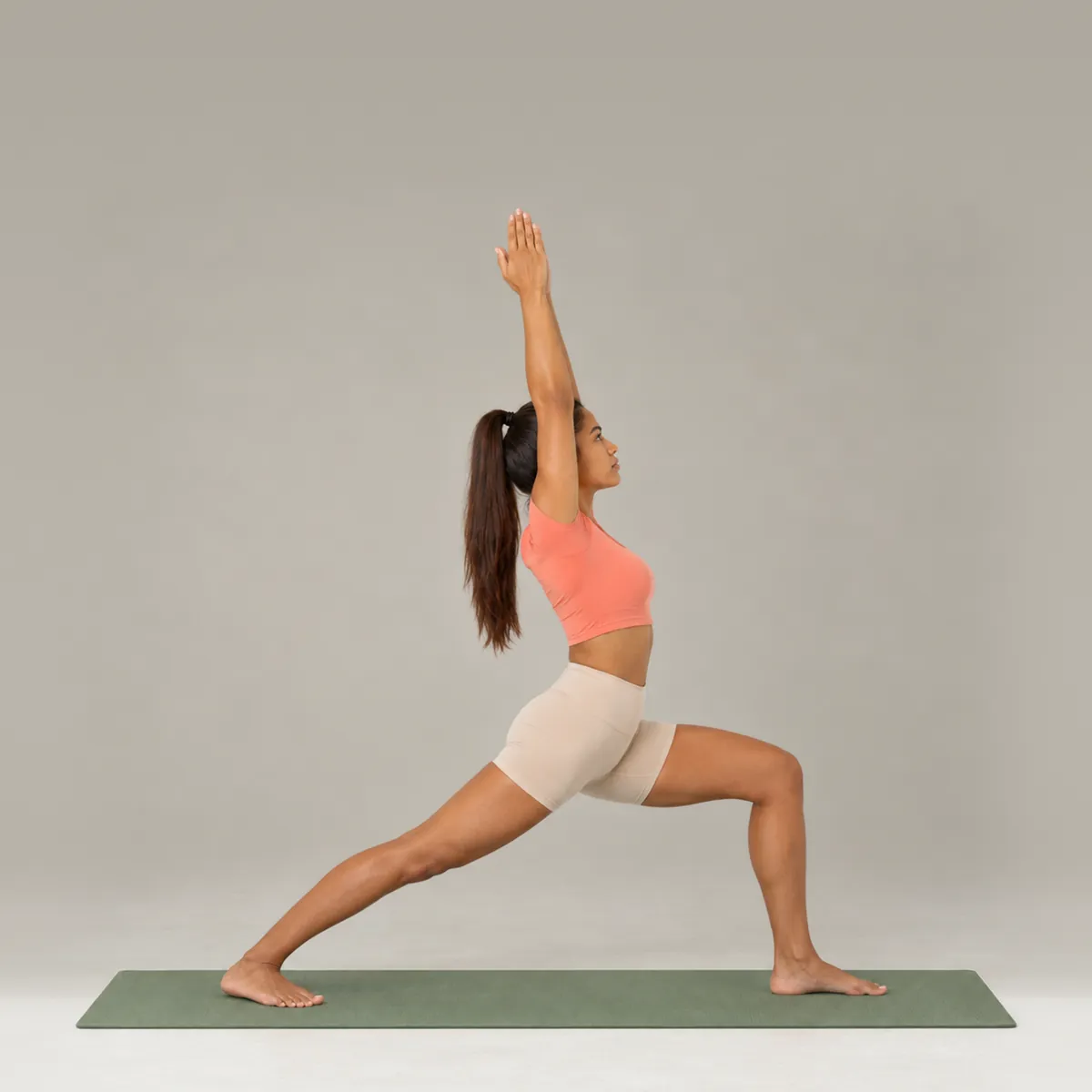 A woman in Warrior I on a green yoga mat, front knee bent and arms reaching overhead