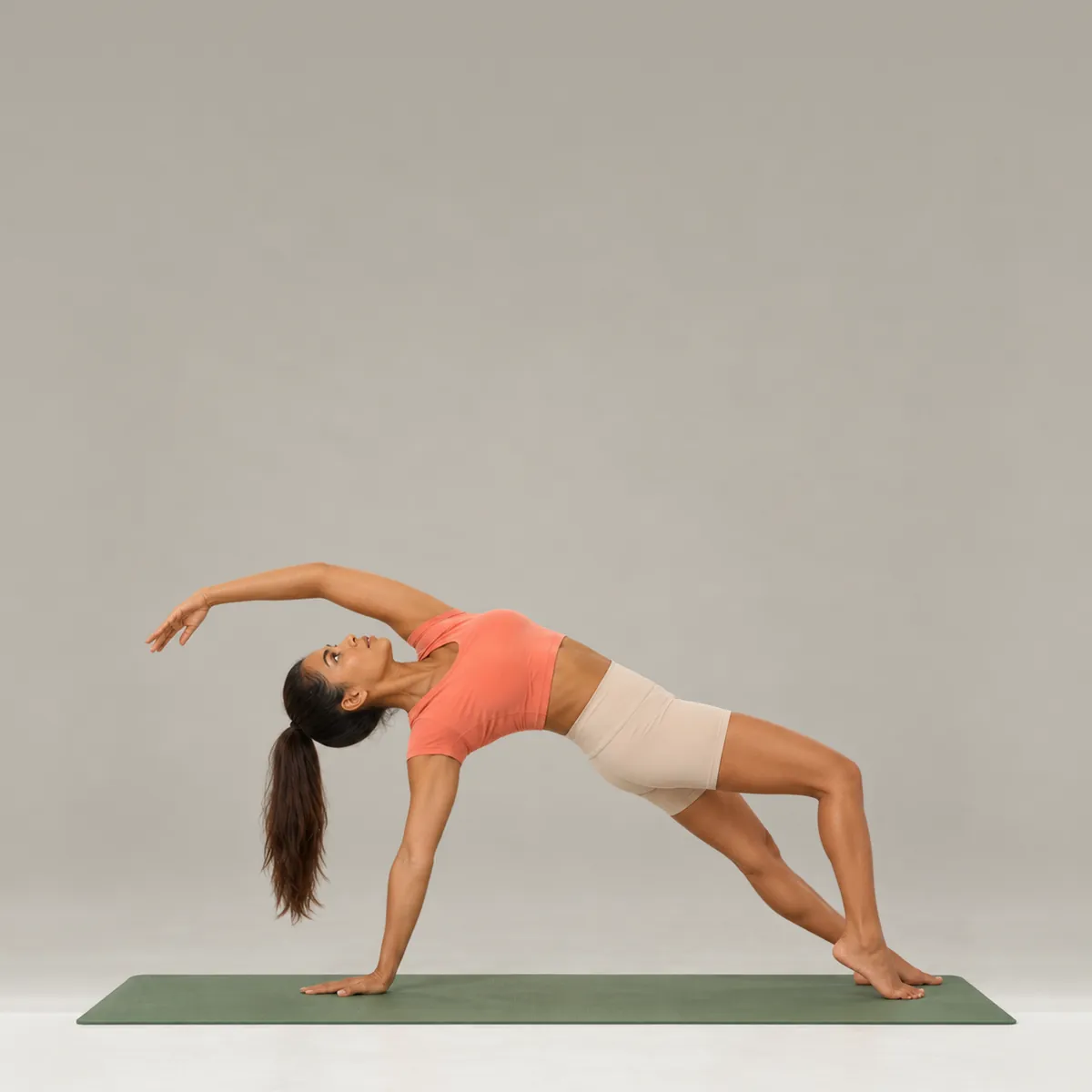 A woman in wild thing on a green yoga mat, chest lifted and top arm sweeping overhead